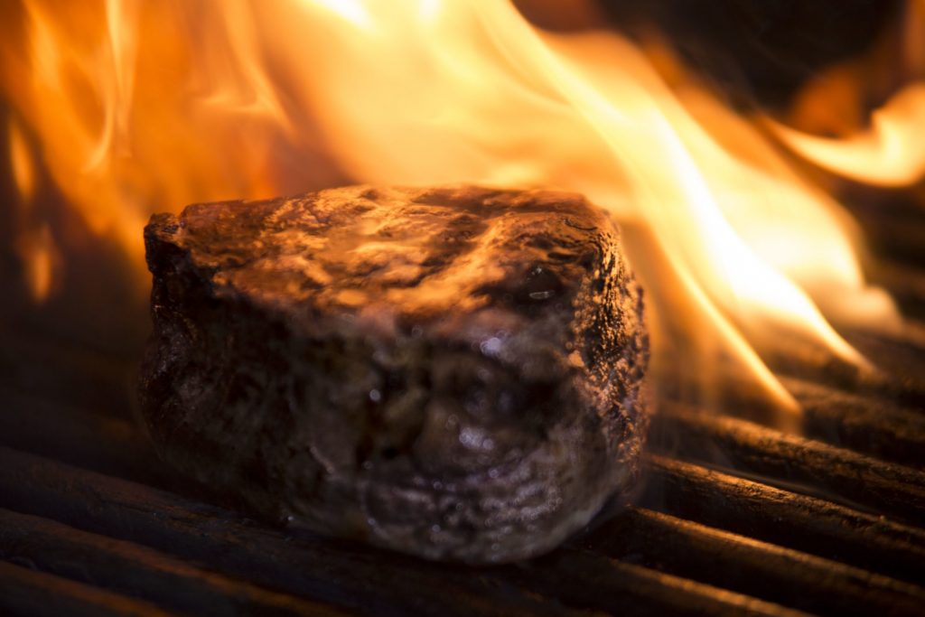 filet steak on a grill with orange flame behind it and all around