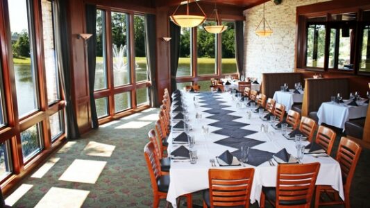 Fancy dining room with a table lined with a white cloth and set for a formal dinner party overlooking a lake with a fountain