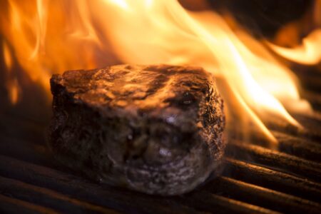 filet steak on a grill with orange flame behind it and all around