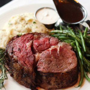 Prime rib meal served on a plate with a loaded potato and green beans